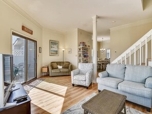 A living room with a sofa, armchair, and a bookshelf. - Walk to Beach | 4BR Beach House w/ Decks + Kitchen (Tower Shores)