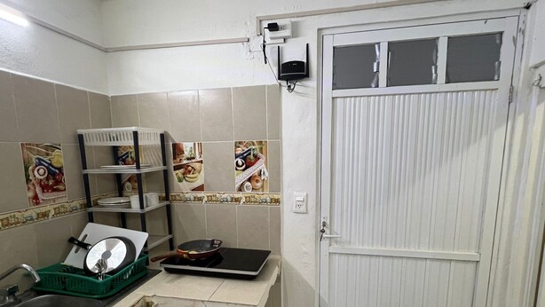 A kitchen with a sink, a stove, and a door. There are shelves with dishes and a window above the door. - Apartment Amanecer Isleño 7 5 min from the beach (Isla Mujeres)