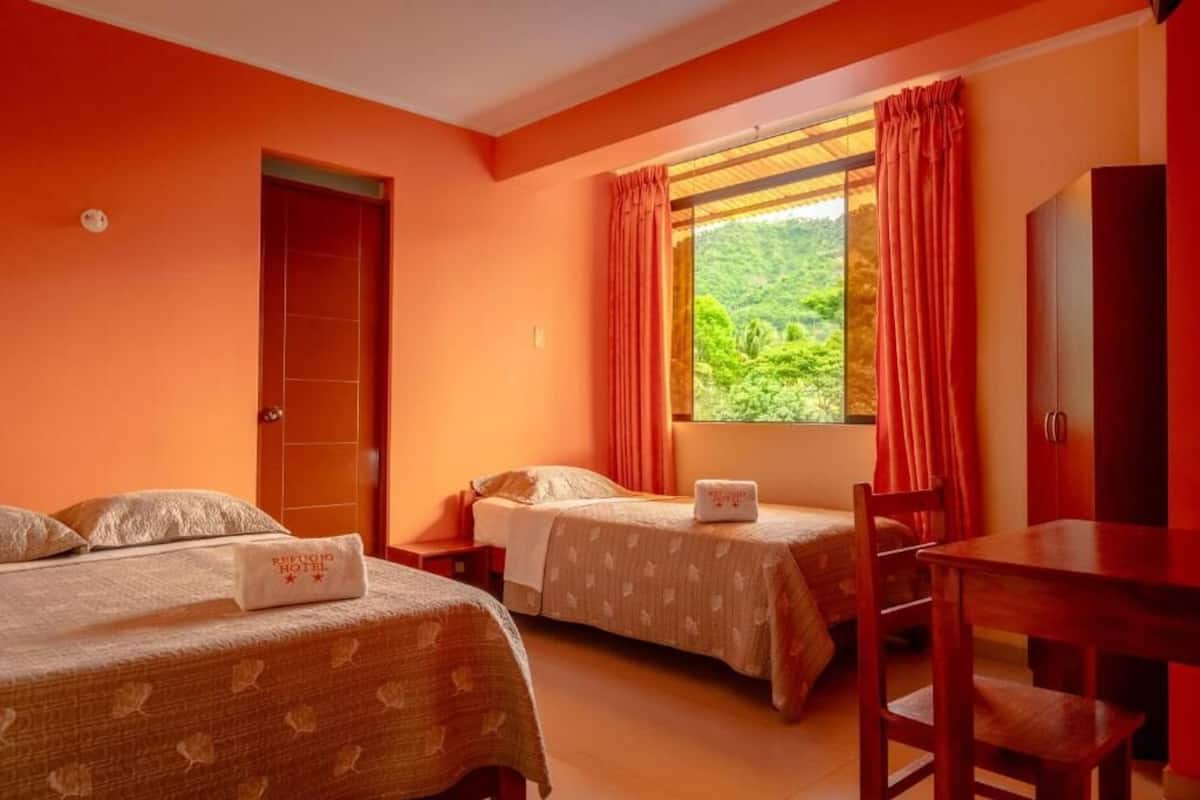 A hotel room with two beds, a wooden desk, and a window with curtains.