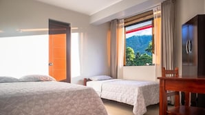 Habitación de hotel con dos camas, una silla de madera, televisor y ventana con vistas a la montaña.