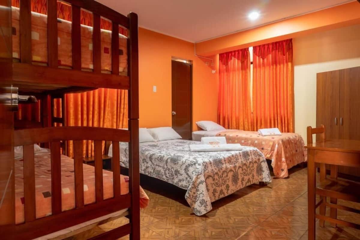 A hotel room with two beds, a wooden wardrobe, and orange curtains.