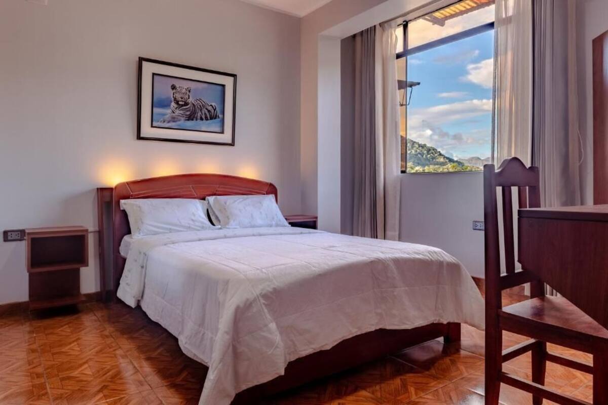 A bedroom with a bed, a nightstand, a chair, and a window with a view of the outdoors.