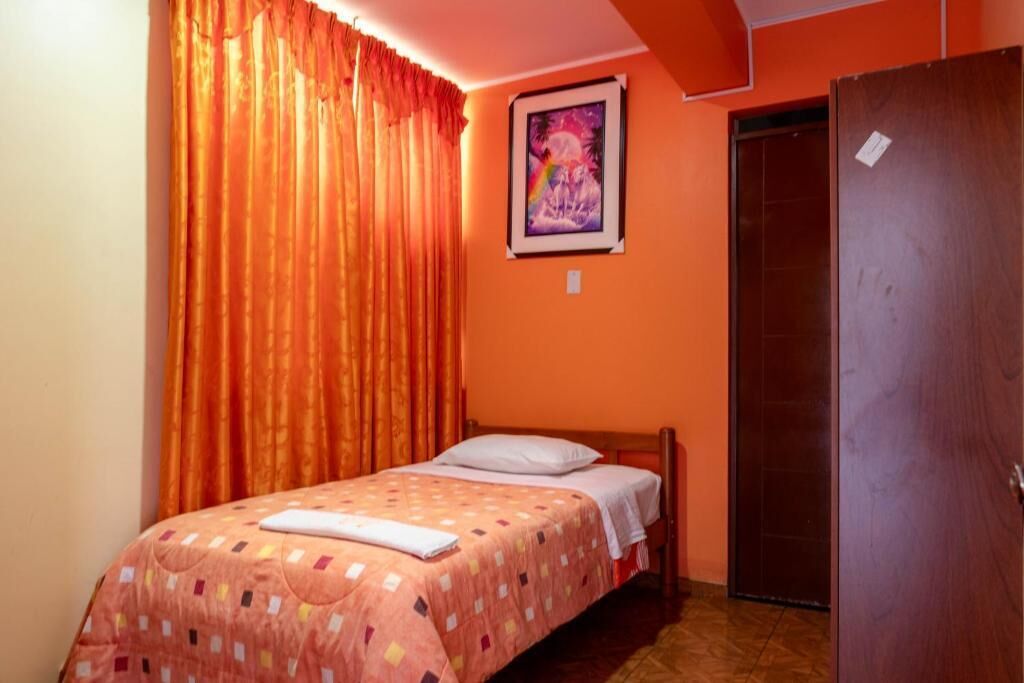 Un dormitorio con una cama, cortinas naranjas, una puerta y un cuadro enmarcado en la pared.