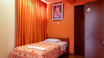 Un dormitorio con una cama, cortinas naranjas, una puerta y un cuadro enmarcado en la pared.