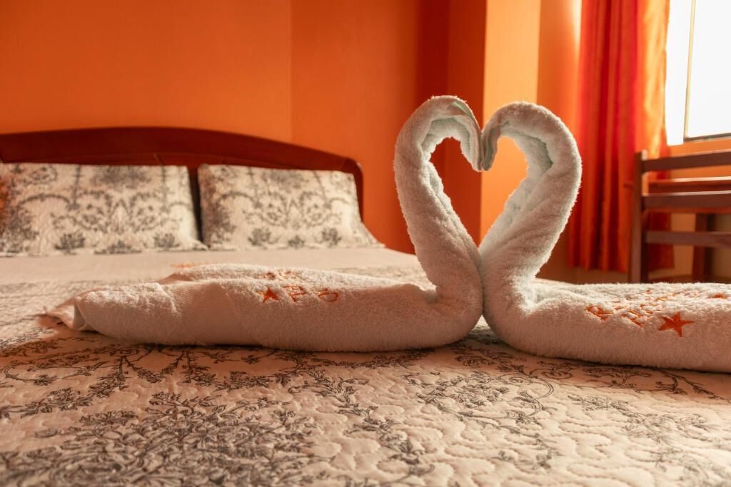 Una cama con una colcha de estampado floral y dos toallas dispuestas en forma de corazón.