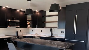Una cucina moderna con mobili scuri, un'isola centrale, due sgabelli da bar e illuminazione a sospensione.