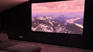 Un home theater con un grande schermo, pareti scure e un'area salotto accogliente con pavimento in moquette.
