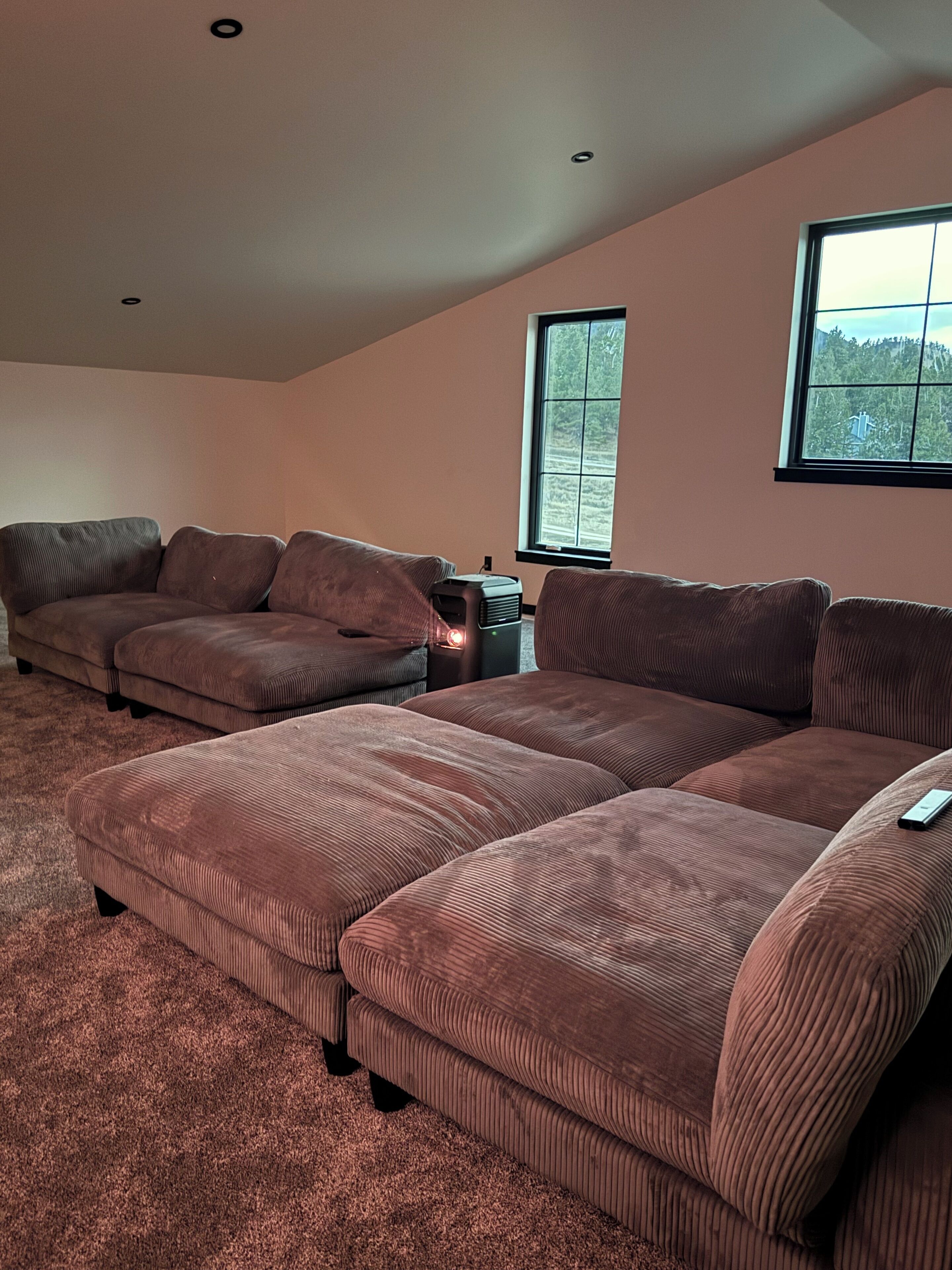 A living room with a sectional sofa, a small table, and a window with a view of trees.