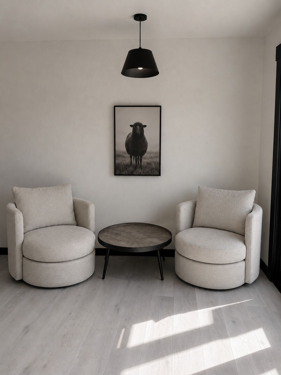 A minimalist room with two armchairs, a small round table, a pendant light, and a framed picture on the wall.