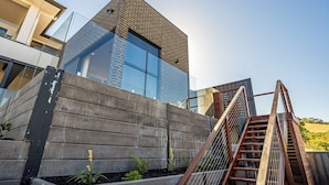 Un bâtiment moderne doté d’une façade en verre remarquable, d’un mur de soutènement en béton et d’un escalier en bois.