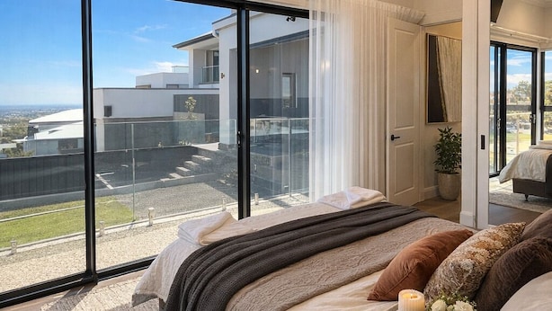Une chambre moderne dotée d’un grand lit, d’un téléviseur à écran plat et offrant une vue sur un quartier résidentiel grâce à de grandes fenêtres.