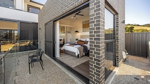 Une maison moderne avec une porte vitrée donnant sur une chambre à coucher équipée d’un lit, d’une chaise et d’un petit balcon.