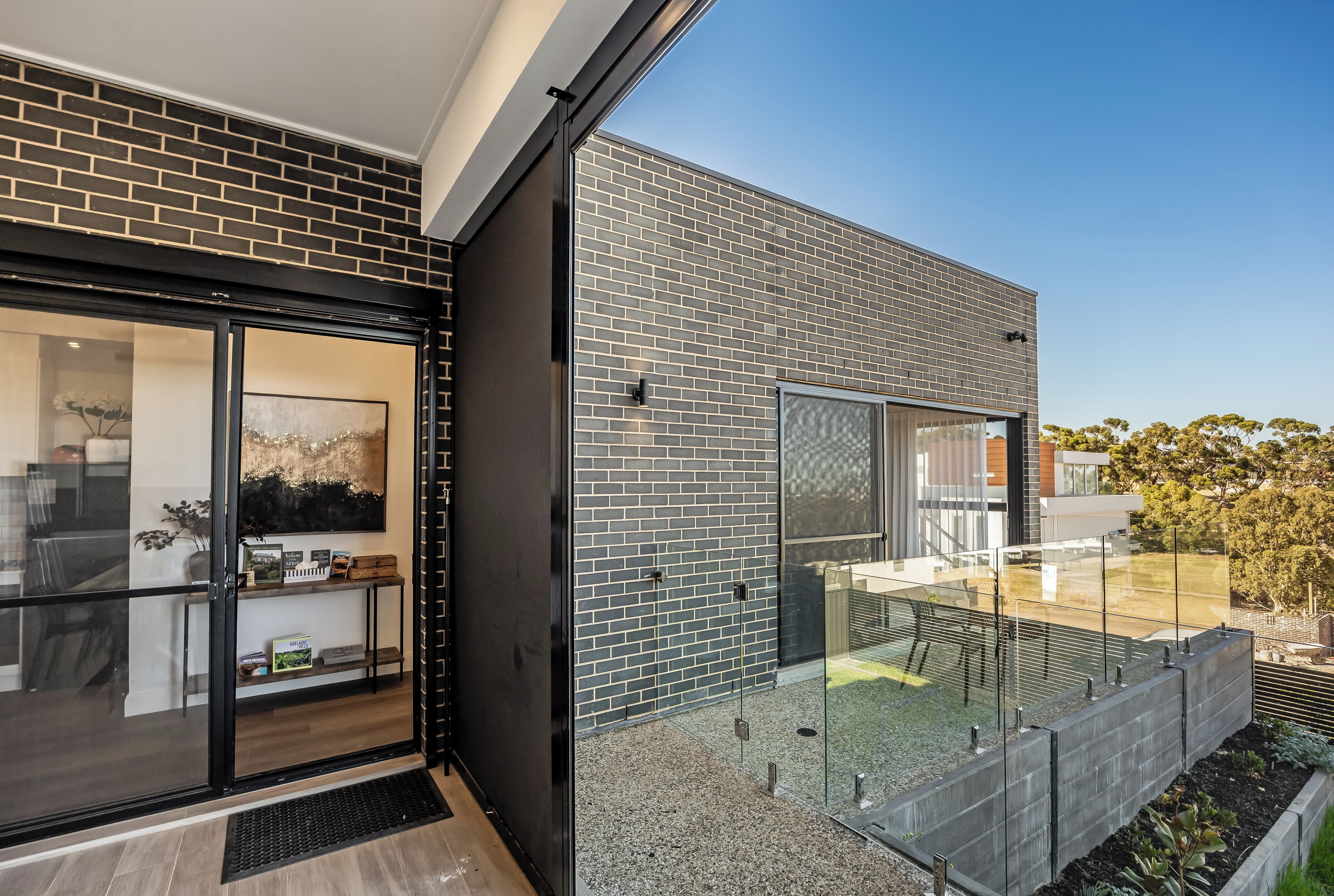 A modern building with a glass door entrance, a brick exterior, and a small outdoor seating area with a glass railing.