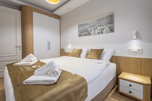 A hotel room with a neatly made bed, a nightstand with drawers, a wall-mounted light, and a cityscape painting. - New Garden View Flat near Cevahir Mall, Şişli (ist)