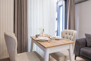A dining area with a wooden table set for two, a beige upholstered chair, and a grey sofa. - New Garden View Flat near Cevahir Mall, Şişli (ist)