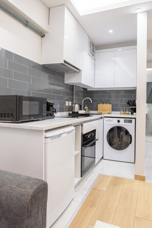 A modern kitchen with white cabinets, a microwave, a coffee maker, a washing machine, and a wooden floor. - New Garden View Flat near Cevahir Mall, Şişli (ist)