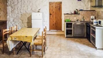 A compact kitchen with a dining table, chairs, a refrigerator, a wooden door, and a small countertop with various items.