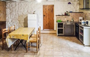 A compact kitchen with a dining table, chairs, a refrigerator, a wooden door, and a small countertop with various items. - Gîte piscine privée dans Mas (Saint-Germain)
