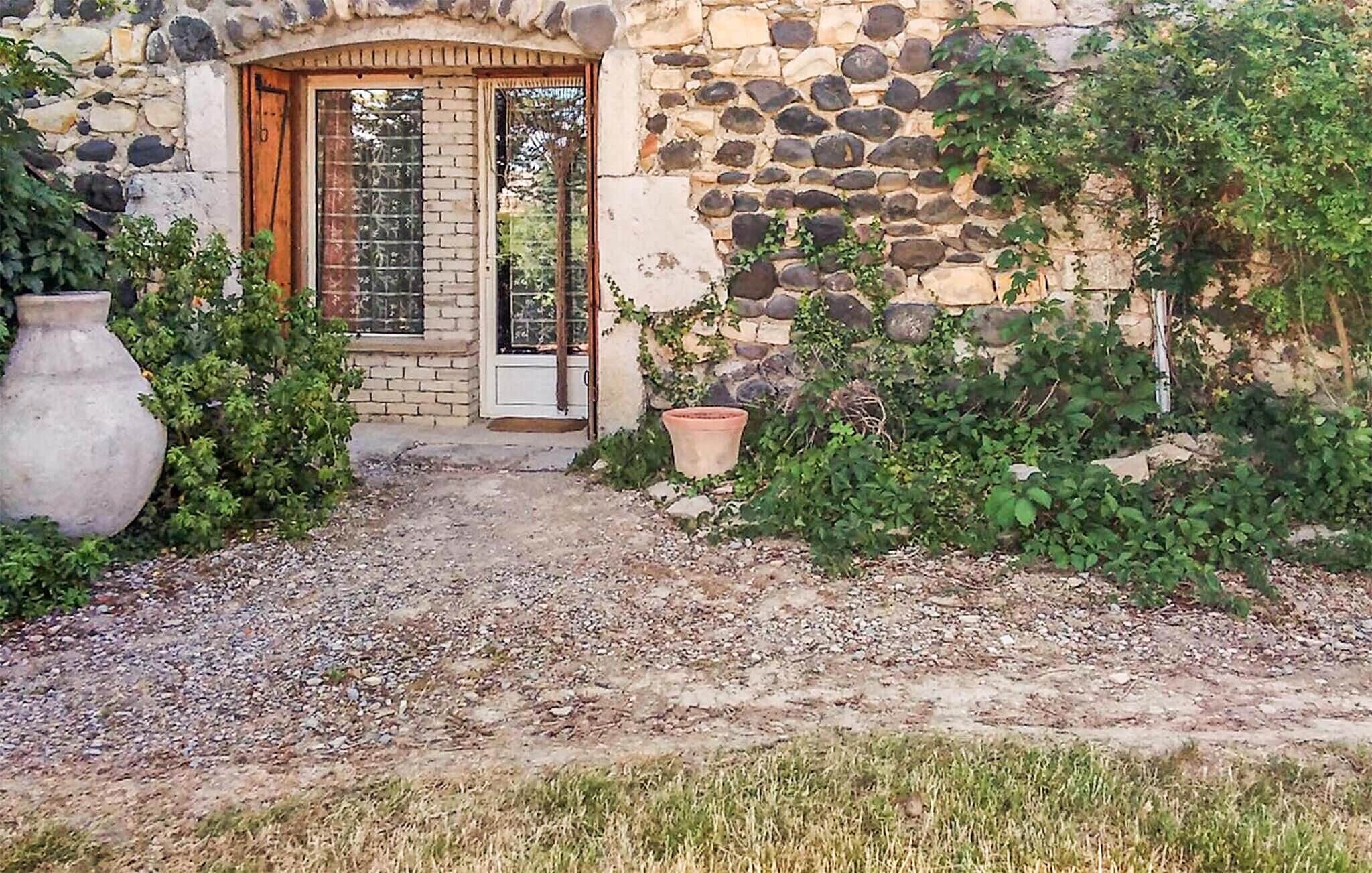 Un edificio de piedra con una puerta de madera, un camino de grava y un jarrón grande.