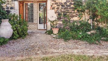 Un edificio in pietra con una porta in legno, un vialetto sterrato e un vaso di grandi dimensioni.