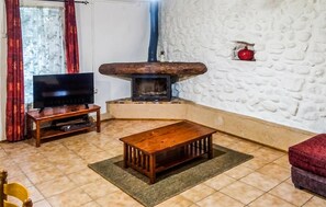 A living room with a television, a fireplace, a wooden table, and a red couch. - Gîte piscine privée dans Mas (Saint-Germain)