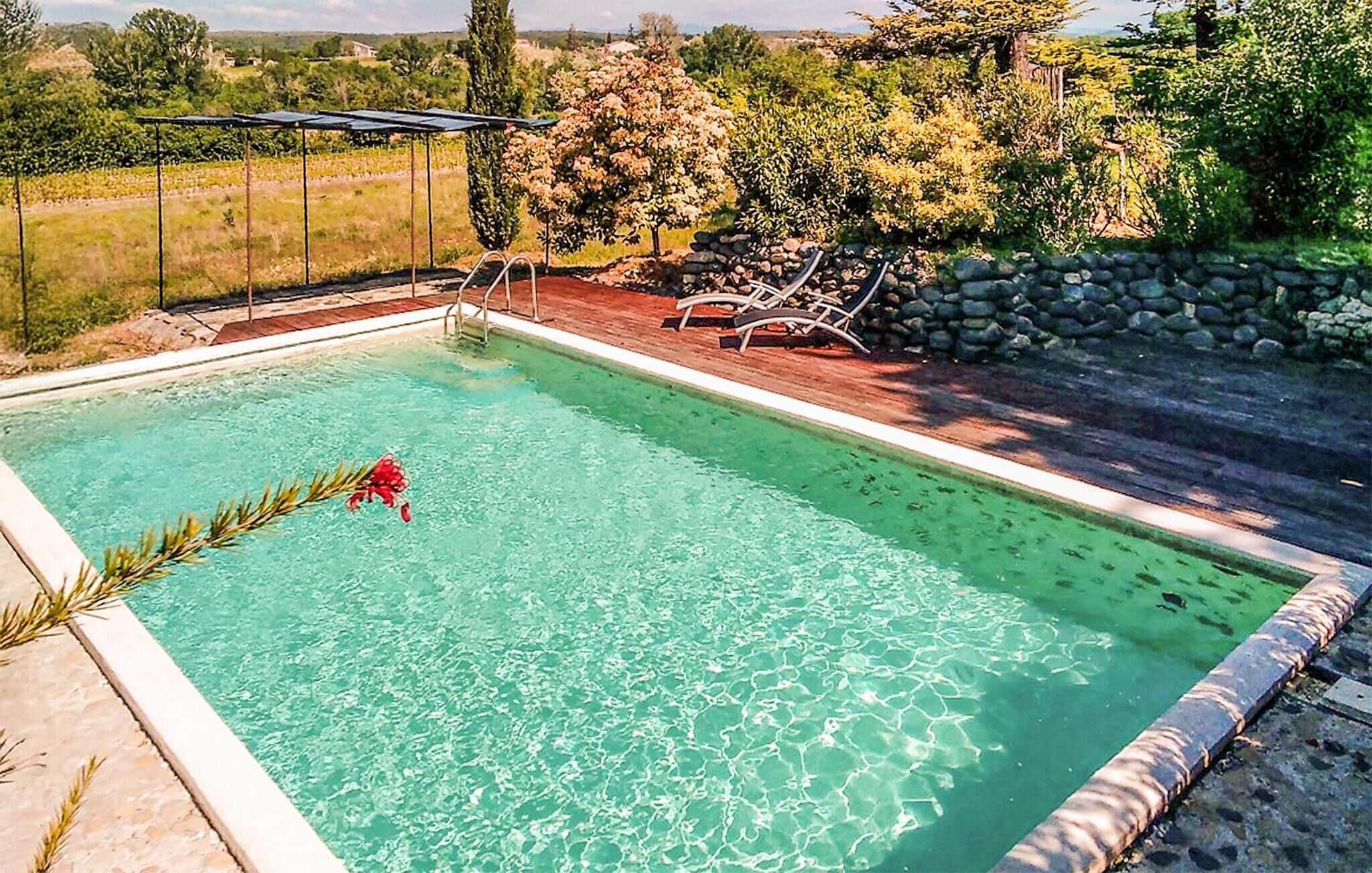 Una piscina rettangolare con acqua cristallina, circondata da un solarium in legno e un muro in pietra.