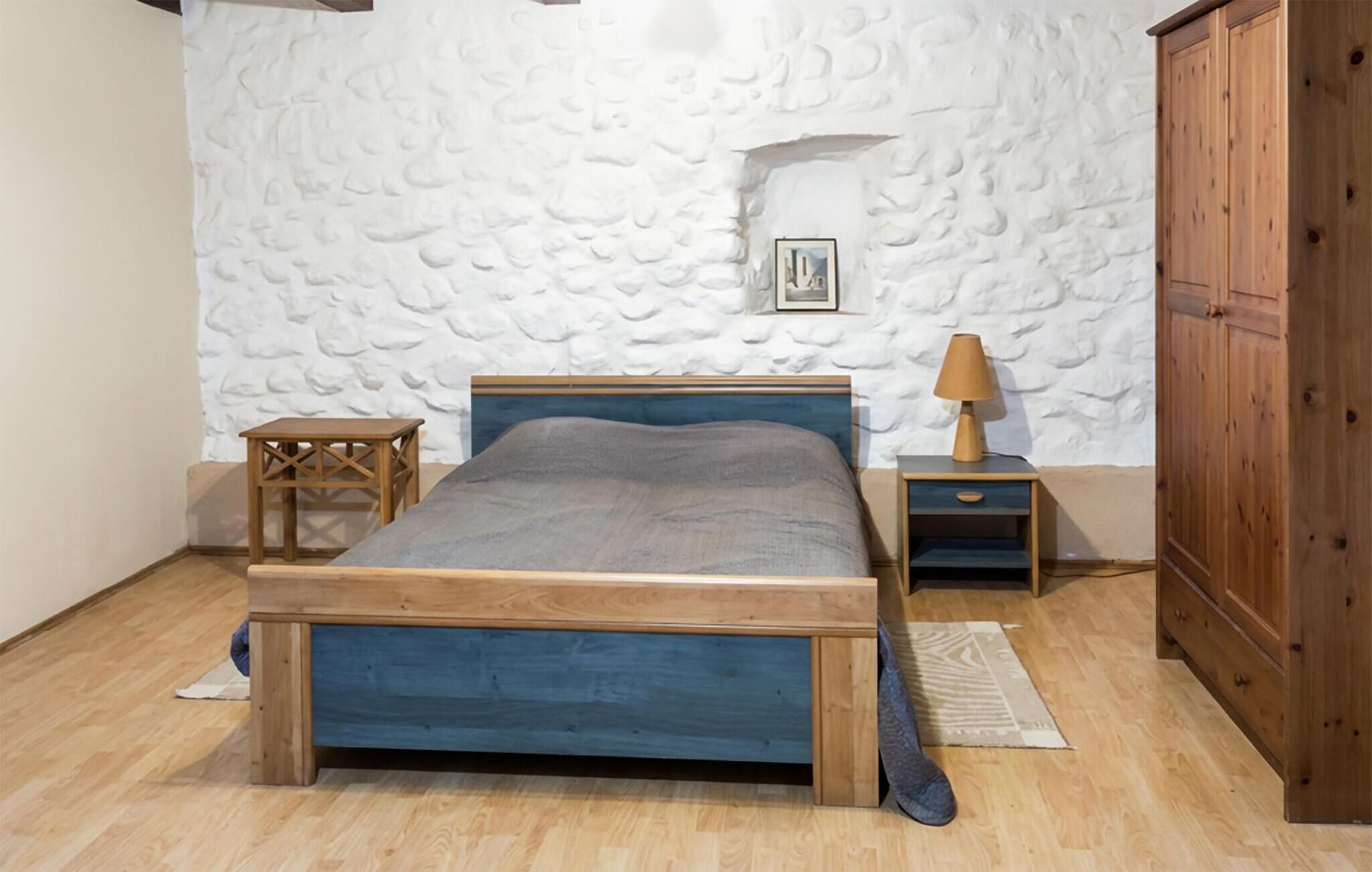 Una camera da letto con un letto in legno, un comodino con una lampada, un piccolo tavolo e un armadio.