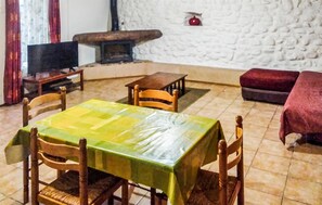 A dining area with a table covered by a green tablecloth, wooden chairs, a stone fireplace, and a red decorative item on the wall. - Gîte piscine privée dans Mas (Saint-Germain)