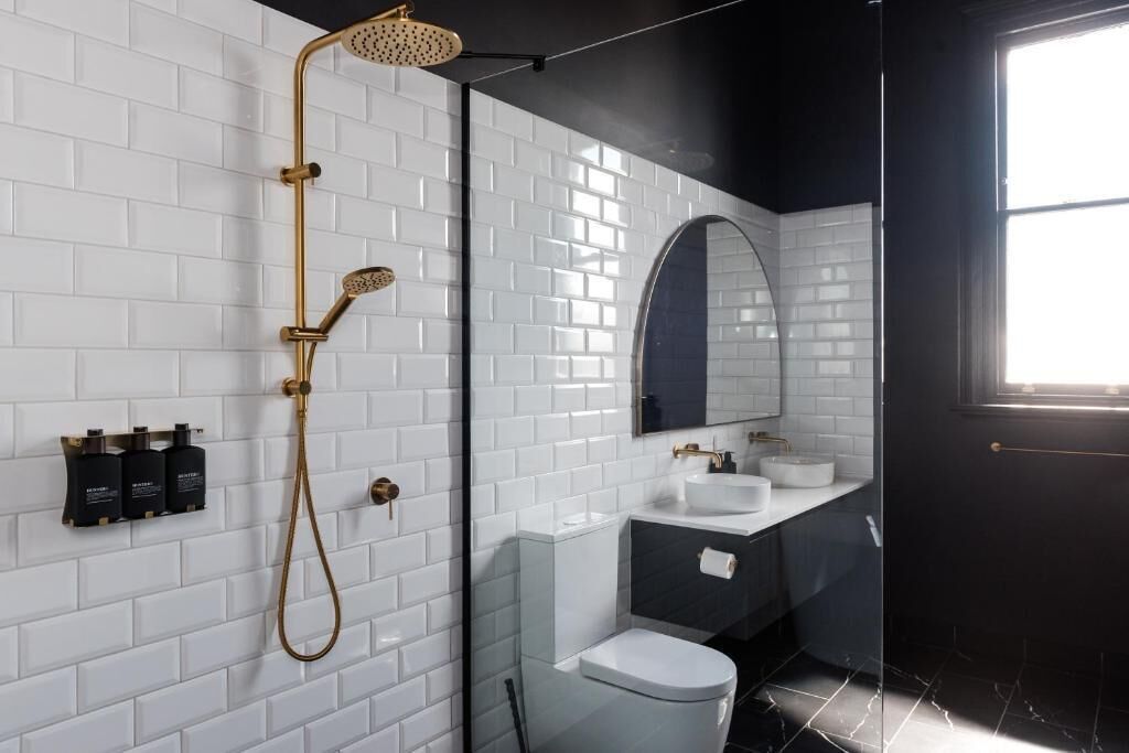 A modern bathroom with white subway tiles, a black shower enclosure, a glass shower door, a white toilet, a vanity with a mirror, and a window.