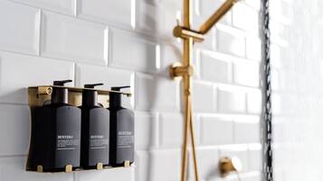 Een badkamer met een witte betegelde muur, een gouden douchekop, en drie zwarte flessen met de naam 'Hunter' op een plank.