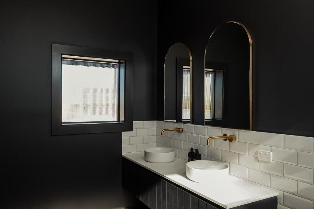 A modern bathroom with two sinks, a window, and a large mirror.