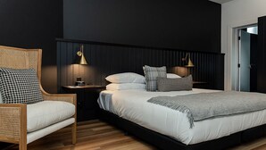 A modern bedroom with a large bed, a wooden chair, a nightstand, and wall-mounted lamps. - The Victoria Rutherglen (Rutherglen)