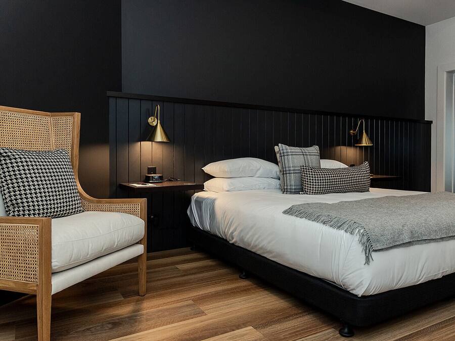 Un dormitorio moderno con una cama grande, una silla de madera, una mesita de noche y lámparas de pared.