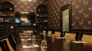 Ein Konferenzraum mit einem langen Tisch, Stühlen, einem Fernseher, Regalen mit Büchern und Dekoration sowie einer Wand mit Muster.