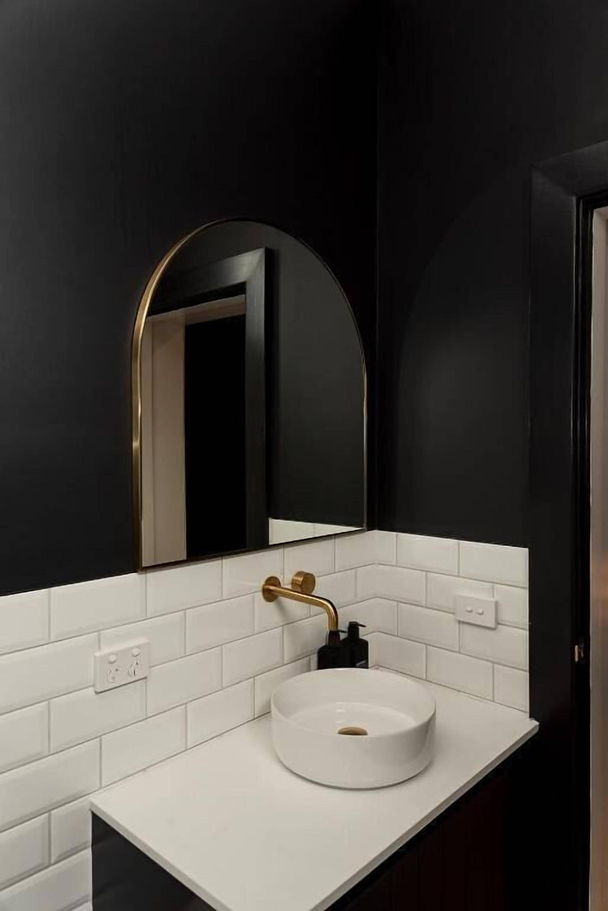 Un baño moderno con un lavabo blanco, paredes negras y un espejo con marco dorado.
