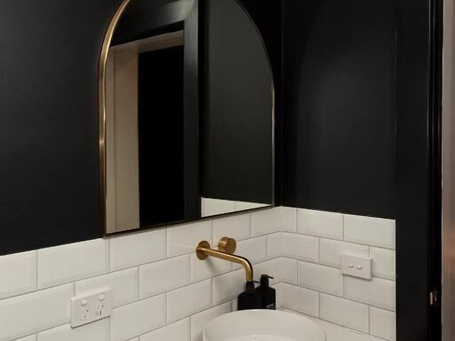 Un baño moderno con un lavabo blanco, paredes negras y un espejo con marco dorado.