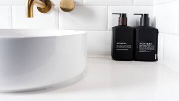 A bathroom with a white sink, gold faucet, and two black Hunter hand soap bottles.