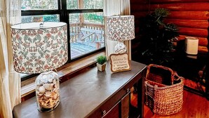 Een houten cabinestil met een groot raam, twee lampen, een bord met 'Welkom', een kleine plant en een geweven mand.