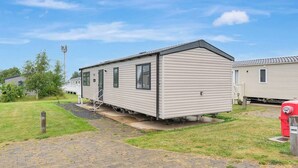 Une maison mobile de plain-pied, dotée d’un toit plat, d’une porte d’entrée et d’un petit porche.
