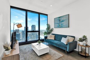 A modern living room with a large window, a blue sofa, a white coffee table, and a city view. - Tallest Building Melbourne - Unbelievable Views (Southbank)