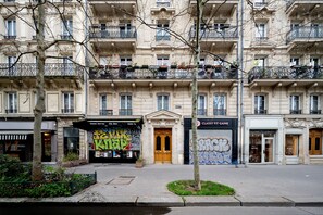 A multi-story building with a classical facade, featuring a central entrance with a wooden door, and balconies with black railings. - Appartement Voltaire - Welkeys (Paris)