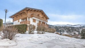 A two-story wooden chalet with balconies, surrounded by snow-covered hills and a clear sky. - Studio L'étoile des neiges - Welkeys (Demi-Quartier)