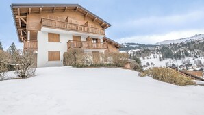 A two-story wooden chalet with balconies, set against a snowy mountain backdrop. - Studio L'étoile des neiges - Welkeys (Demi-Quartier)
