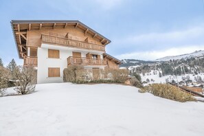 Eine zweistöckige Holzhütte mit Balkonen vor einer verschneiten Berglandschaft.