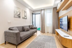 Ein modernes Wohnzimmer mit einem grauen Sofa, einem Flachbildfernseher an einer Holzwand und einem gemusterten Teppich.
