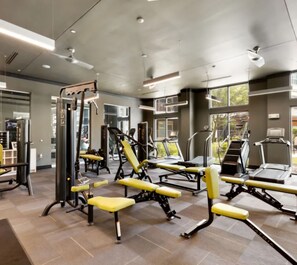 Ein modernes Fitnessstudio mit unterschiedlichen Trainingsgeräten, großen Fenstern und einem sauberen, gefliesten Boden.