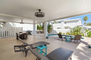 A covered outdoor area with a pool, lounge chairs, and a dining table. - The Sea Pearl (Holmes Beach)