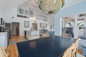 A spacious dining area with a large table and wicker chairs, a kitchen with modern appliances, and a decorative chandelier. - The Sea Pearl (Holmes Beach)