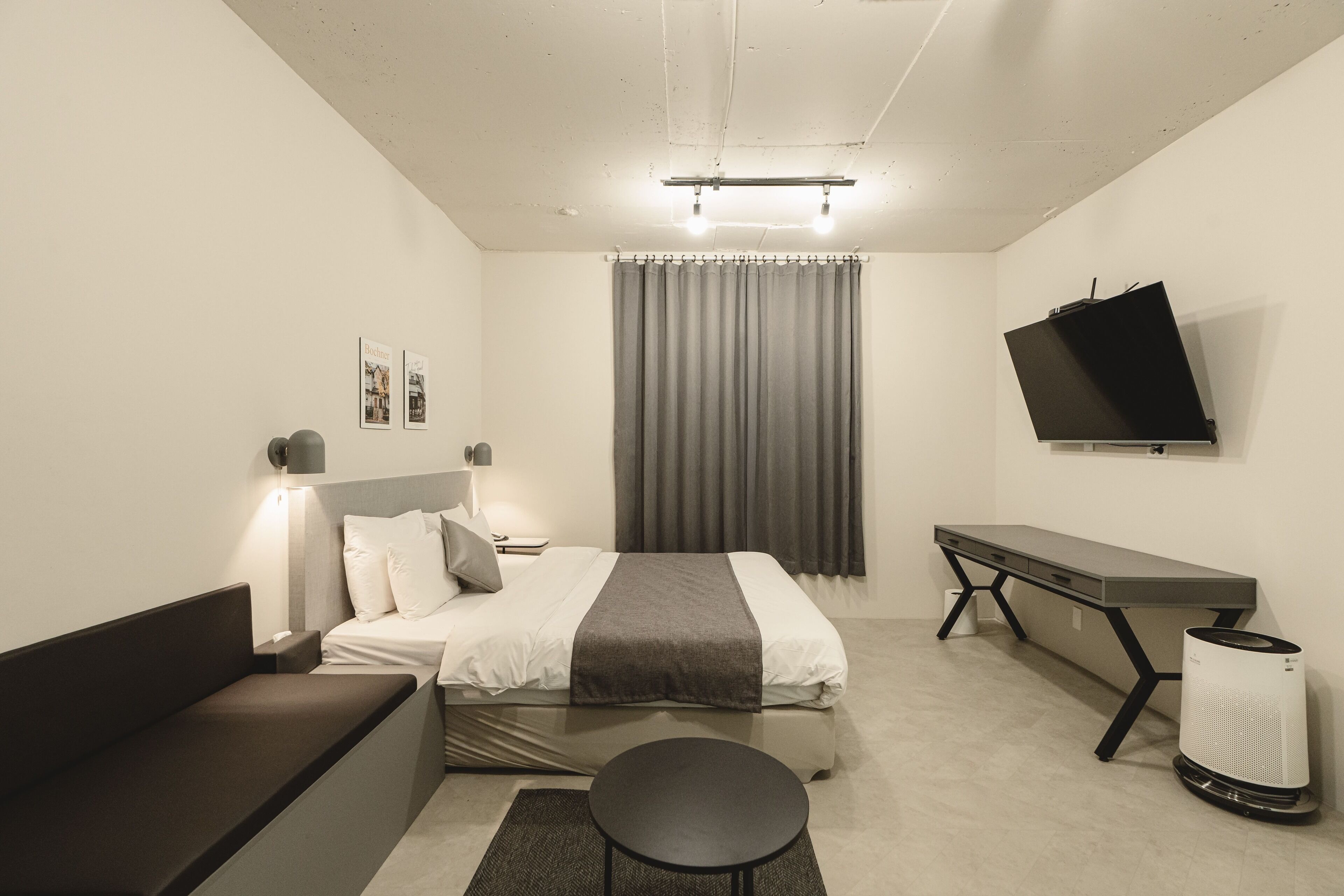 A modern hotel room with a bed, bedside table, lamp, TV, and a desk.
