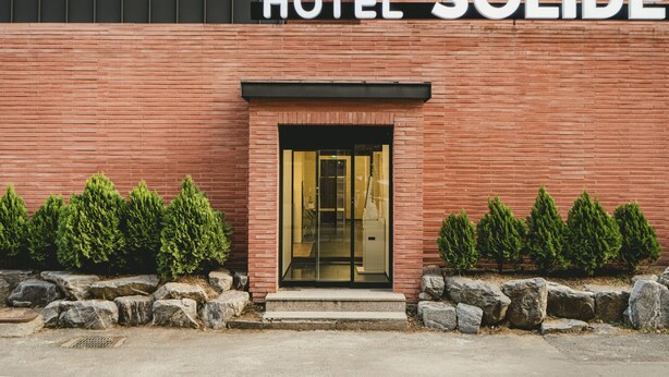 Entrada de hotel com fachada de tijolos, porta de vidro e placa com a inscrição 'HOTEL SOLIDE'.